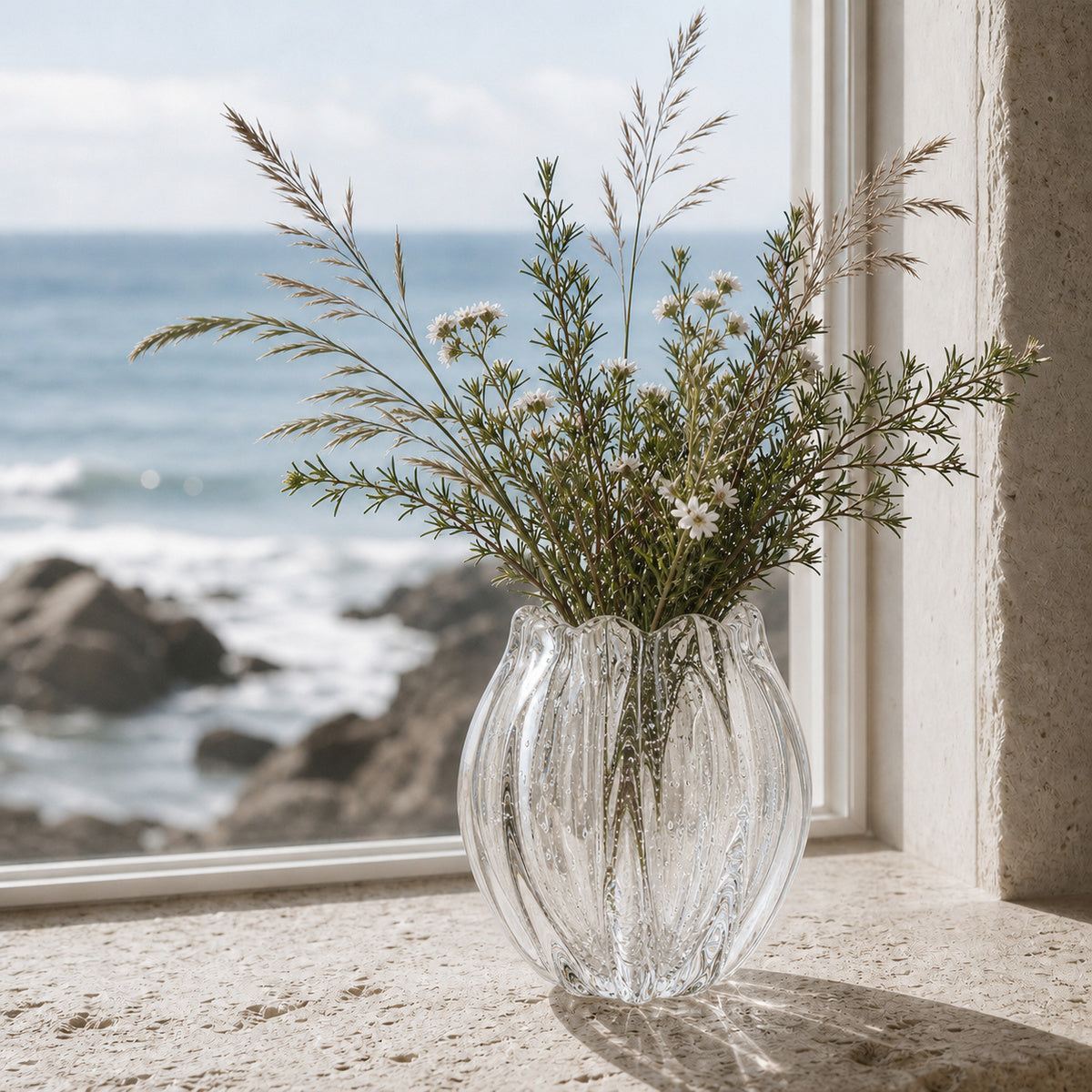 Clear glass Onda Vase Calyx with dried plants on a windowsill with ocean view