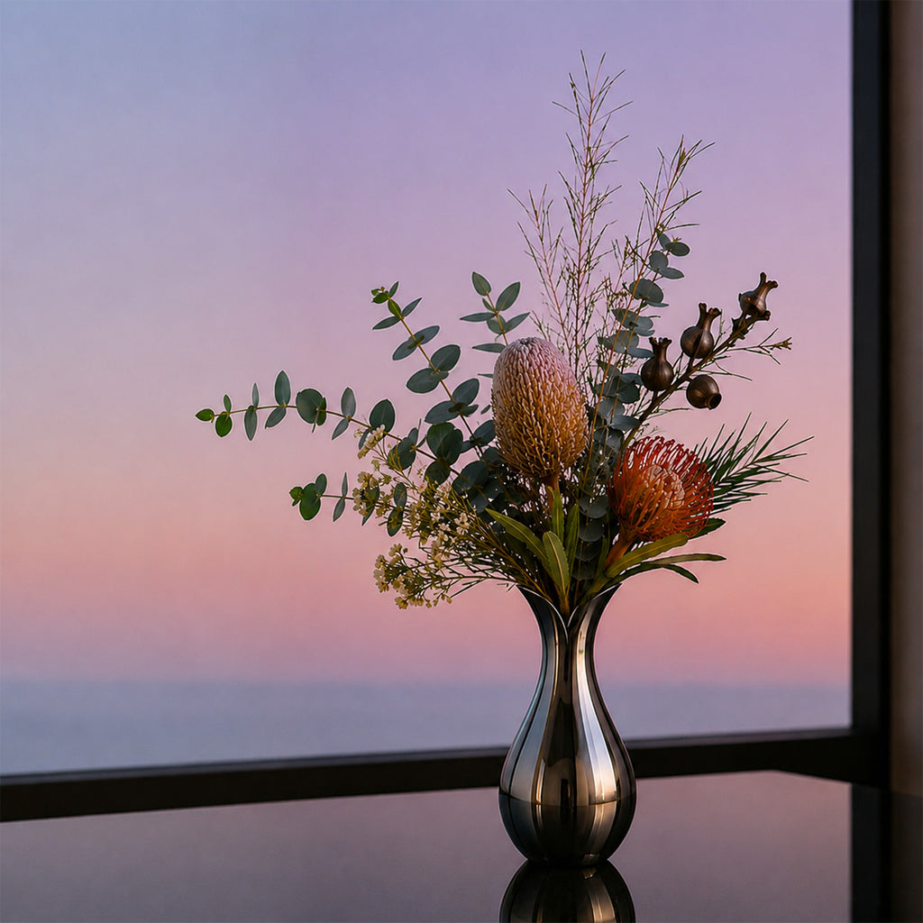 Silver stainless steel modern vase with flowers on a reflective surface at dawn