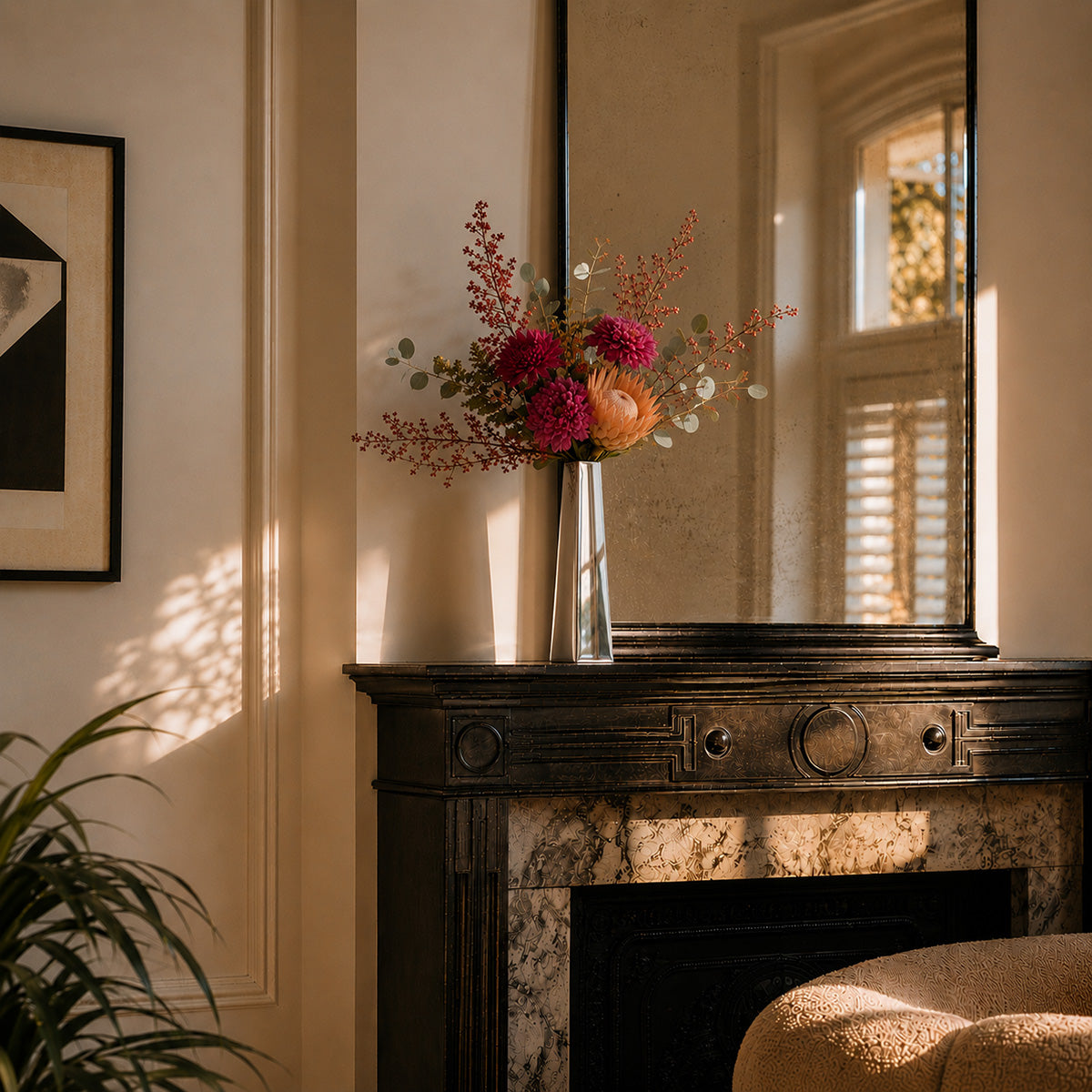 Decorative metal vase with flowers on a marble fireplace mantel in a sunlit art deco room.
