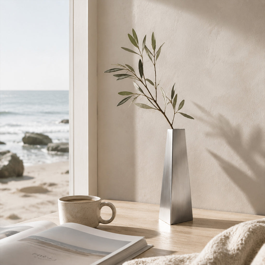 Silver vase with branches on a windowsill with a view of the ocean.