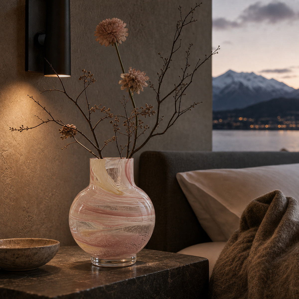 Decorative pink glass vase with flowers on a bedside table in a cozy bedroom room with mountains in the background