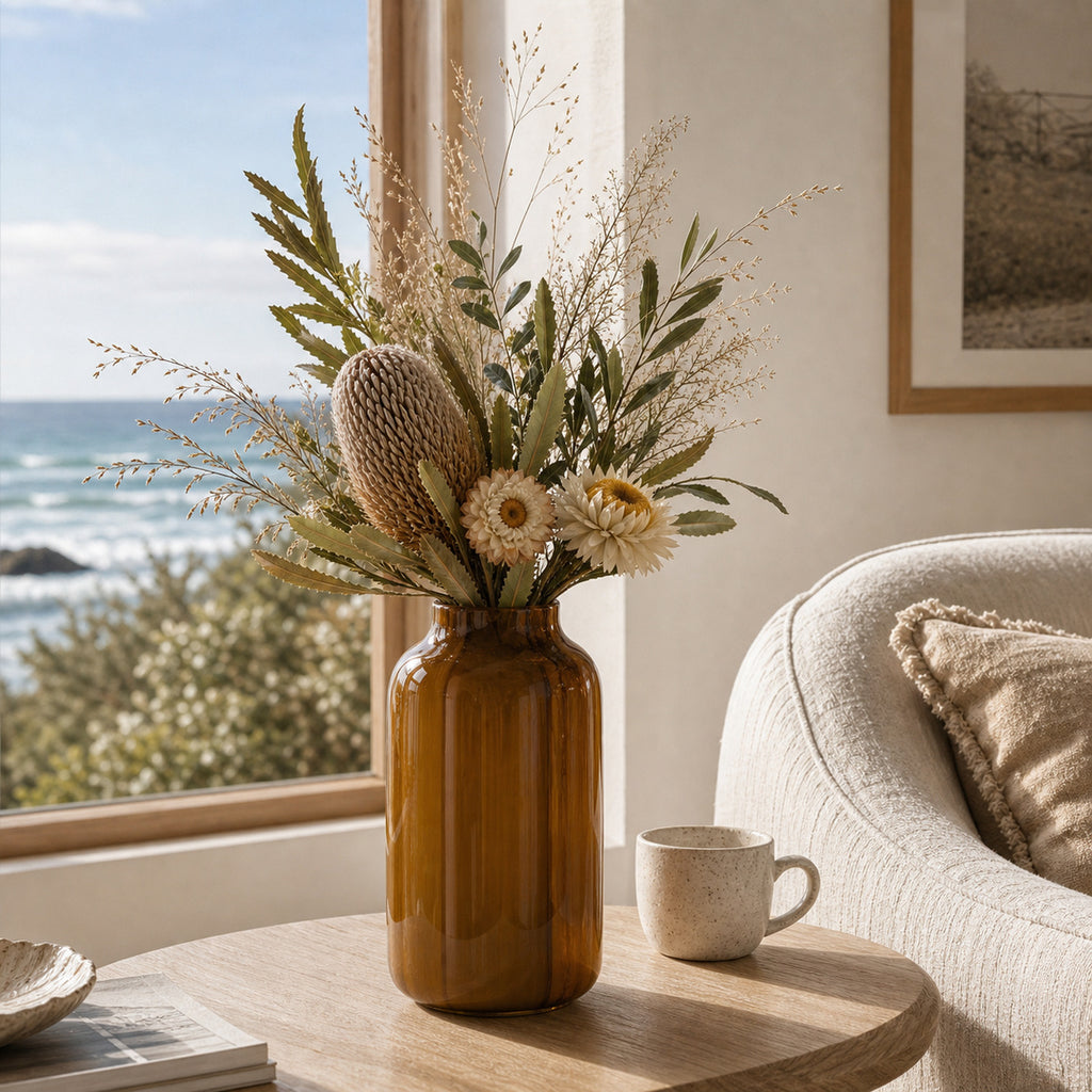 Bouquet of dried flowers in a brown translucent glass modern vase on a table with a view of the ocean in Lorne.