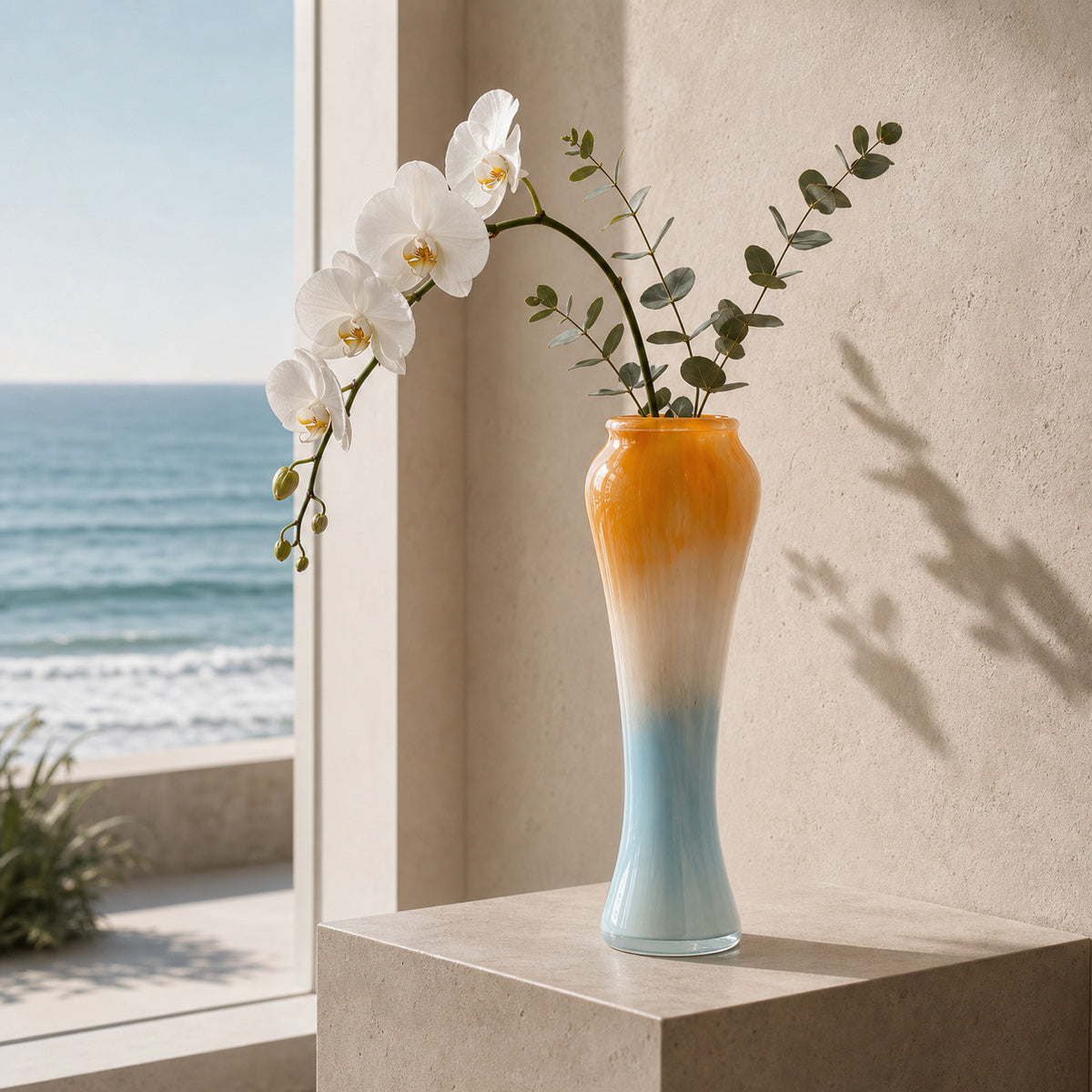 Gradient Glass Vase - Onda Vase Solis displaying a white orchid and eucalyptus leaves on a plinth overlooking the ocean.