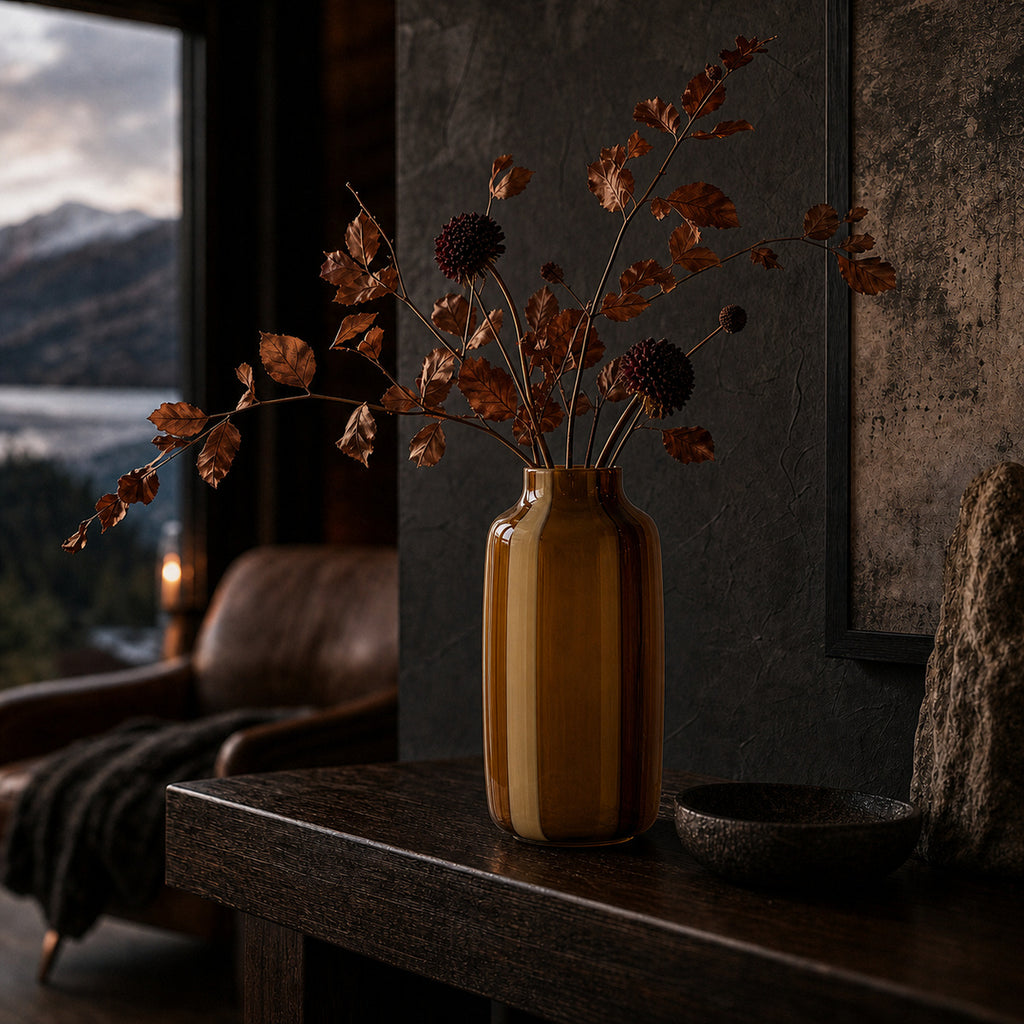 Amber striped glass vase - Onda Vase Toffane displaying dried burgundy alliums and copper foliage on a dark wood console in a moody rustic cabin with mountain views.
